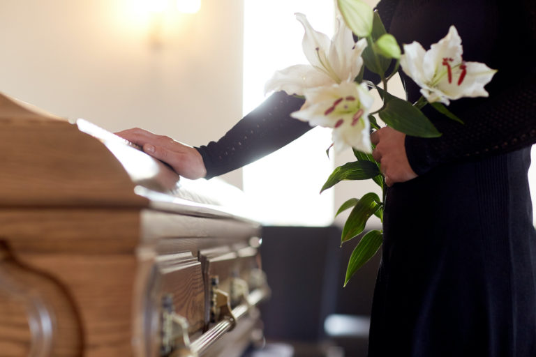 Woman holding flowers next to casket
