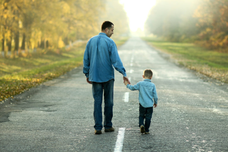 Father and toddler son walking down the road