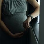 Photo of pregnant woman in grey dress looking at watch