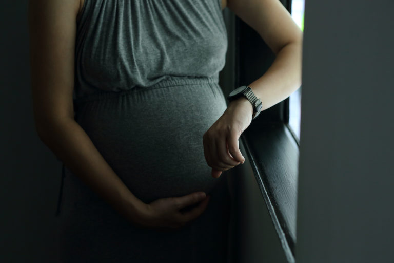 Photo of pregnant woman in grey dress looking at watch