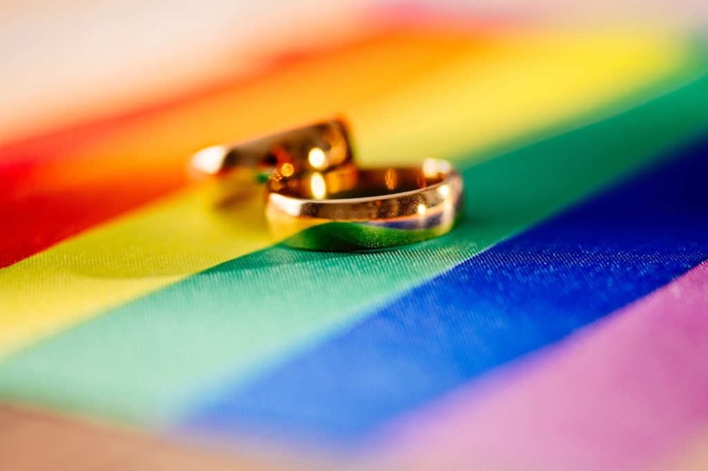 Two gold wedding rings on rainbow lgbt flag. Homosexual marriage.