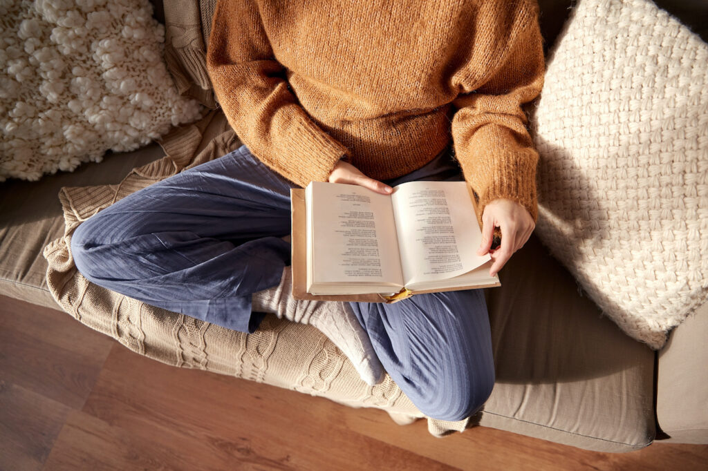 woman in warm sweater reading book at home