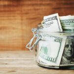 Dollar bills in glass jar on wooden background. Saving money concept.