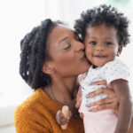 Smiling Black mother kissing baby daughter on cheek