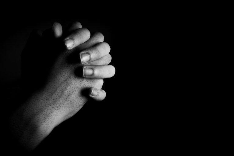 Praying hands is in the dark with light on the hands.