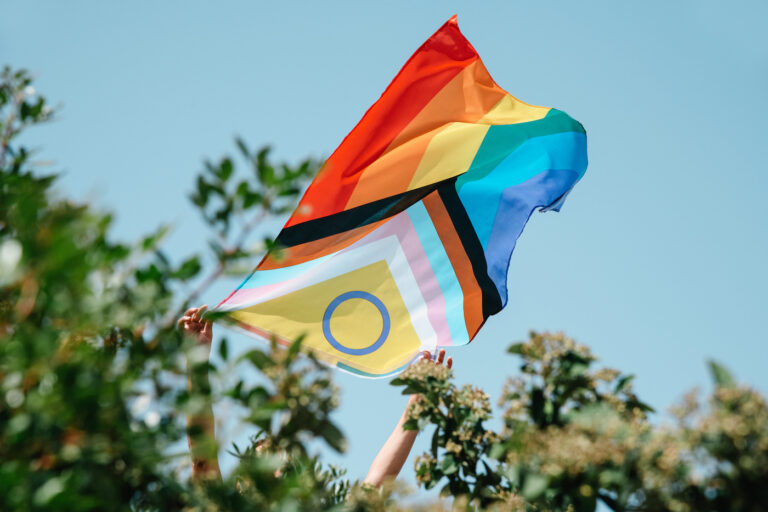 closeup of a man showing an intersex-inclusive progress pride flag peeping out from a bush