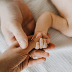 Father and mother holding small newborn baby hand, closeup.