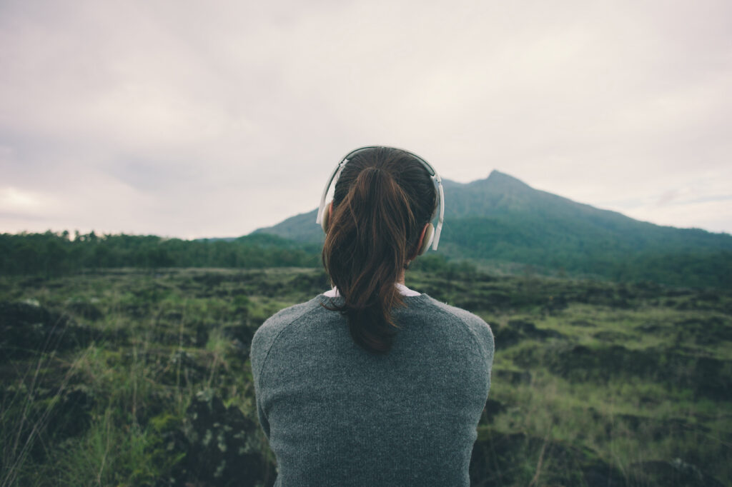 Woman in headphones listening music in nature and at the mountain (intentional pale color style)