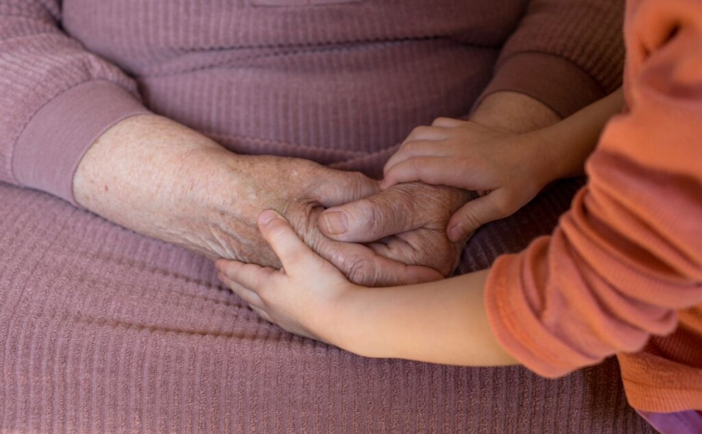 old person in a wheelchair holding a small child's hands