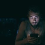 young man looking at phone in a dark room, alone